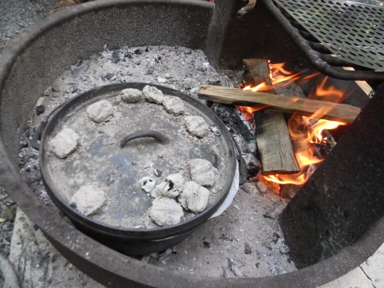 A cast iron Dutch oven with hot coals on the lid, cooking over a campfire