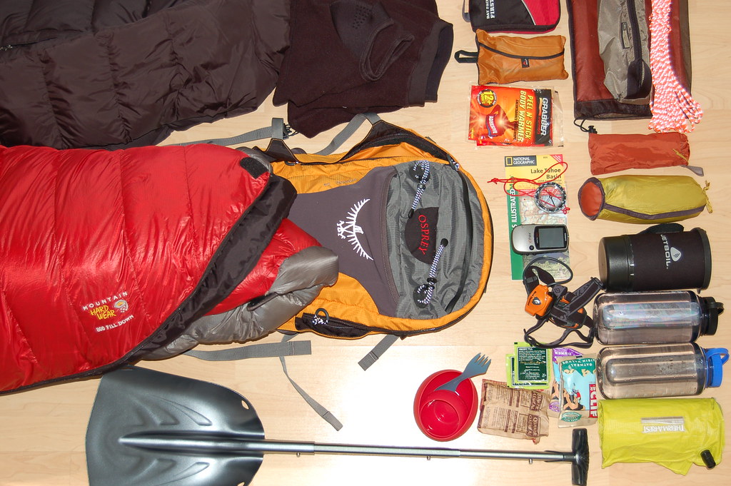 Camping gear including a sleeping bag, backpack, and cooking supplies laid out for packing