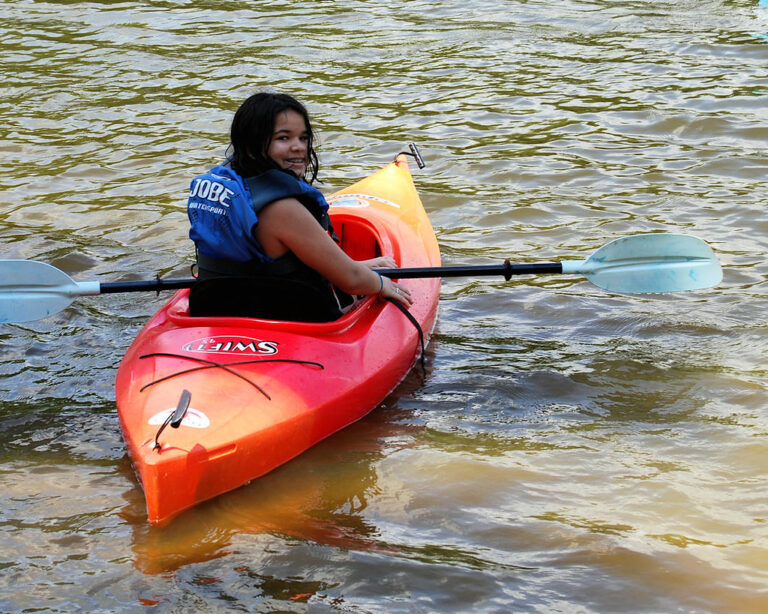 A child in a life jacket paddling a kayak on calm lake water