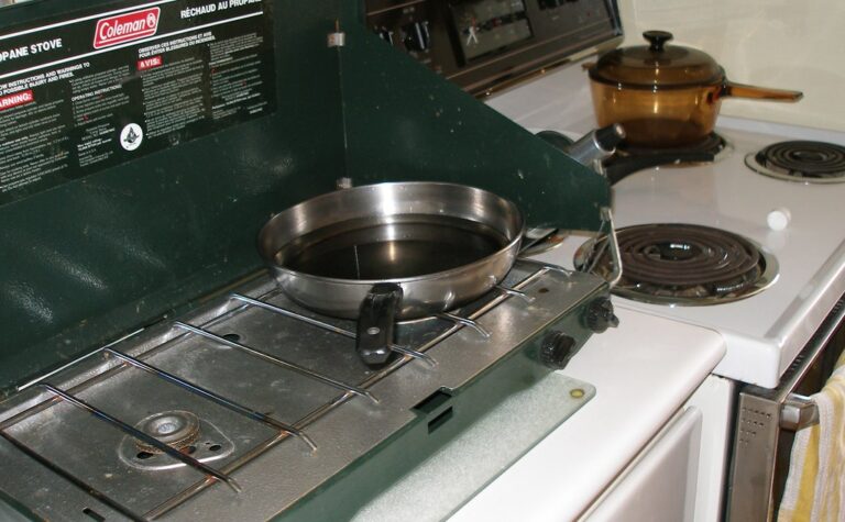 A two-burner propane camp stove with a skillet on top