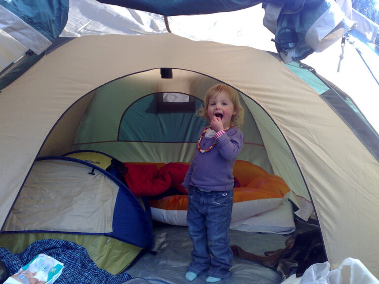 A child standing inside a tent with a sleeping bag and sleeping pad visible